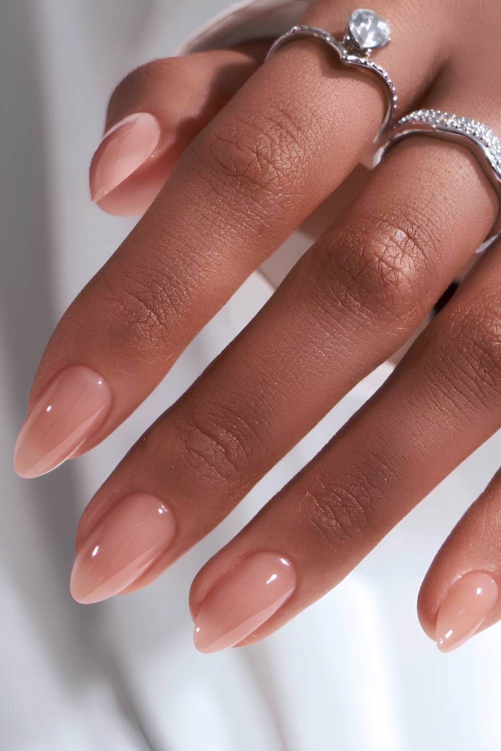 Minimalist nude almond manicure on a hand with pearl ring