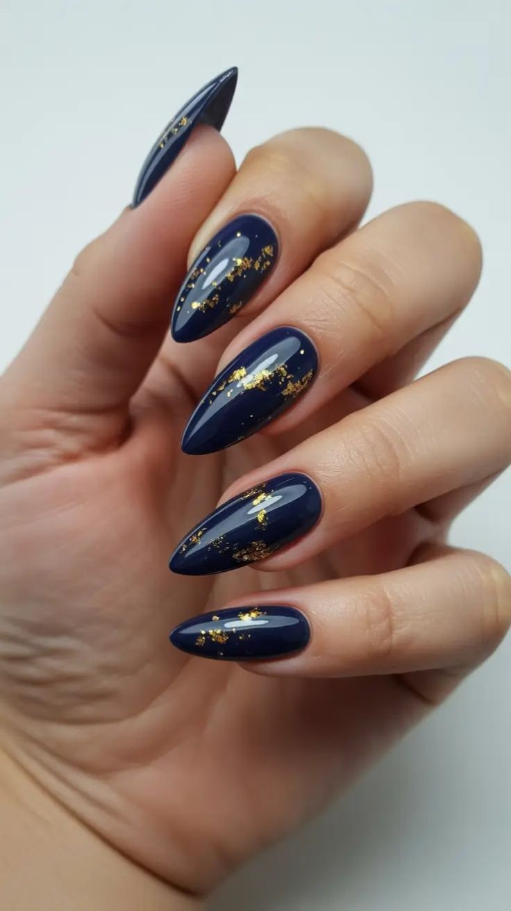 Glossy navy stiletto nails with scattered gold leaf flakes