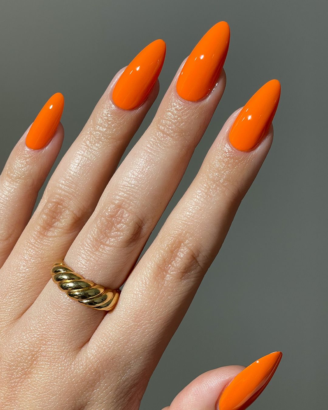 Solid neon orange almond nails with chunky gold ring