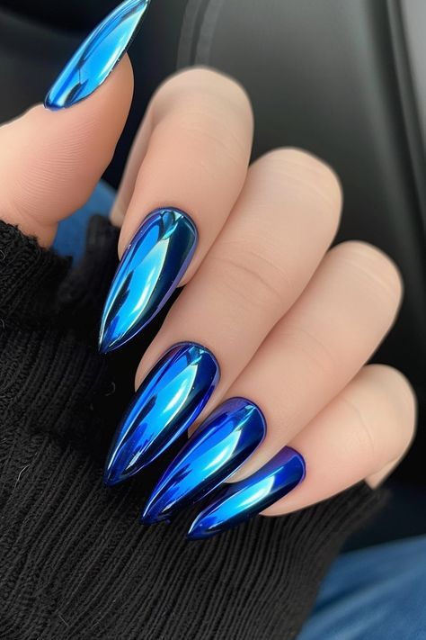 Mirror sapphire blue chrome stiletto nails against a black knit sleeve