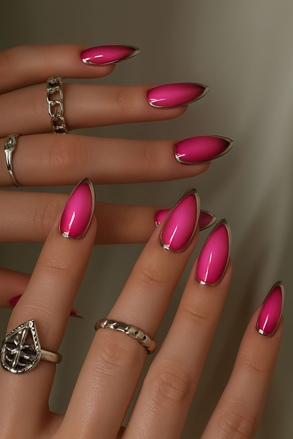 Hot pink almond nails with metallic silver chrome rim outlining each nail, multiple silver rings
